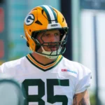 Tucker Kraft - Ein Footballspieler, der einen Helm und ein Trikot der Green Bay Packers mit der Nummer 85 trägt, steht bei Tageslicht auf dem Spielfeld, während einige Fans gespannt seine Leistung verfolgen. Alt-Text wurde KI-generiert.