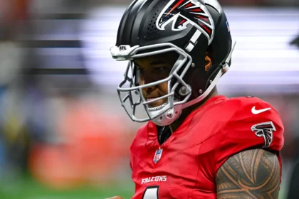 Tua Tagovailoa - Ein Footballspieler der Atlanta Falcons in Trikot und Helm auf dem Spielfeld, konzentriert vor einem Spiel, während die Nachricht die Runde macht, dass Tua wegen einer Schrägmuskelverletzung ausfällt. Alt-Text wurde KI-generiert.