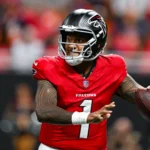 Tua Tagovailoa - Ein Footballspieler in einem roten Trikot und Helm der Atlanta Falcons macht sich während eines Spiels bereit, den Ball zu werfen, und demonstriert damit die hohe Konzentration, die die Falcons im Training an den Tag legen. Alt-Text wurde KI-generiert.