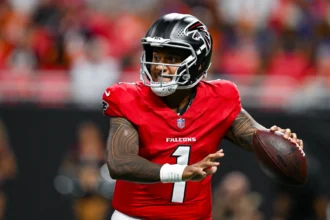 Tua Tagovailoa - Ein Footballspieler in einem roten Trikot und Helm der Atlanta Falcons macht sich während eines Spiels bereit, den Ball zu werfen, und demonstriert damit die hohe Konzentration, die die Falcons im Training an den Tag legen. Alt-Text wurde KI-generiert.