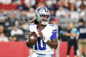 Ein Footballspieler der Dallas Cowboys in Spielkleidung bereitet sich während eines Spiels auf einen Pass vor, während Berichte auftauchen, wonach die Cowboys Joe Milton entlassen haben. Alt-Text wurde KI-generiert.