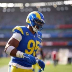 Myles Garrett - Ein Footballspieler in blau-gelbem Trikot und Helm steht während eines Spiels auf dem Spielfeld; im Hintergrund sind das Stadion und die Zuschauer zu sehen. Bericht Garrett wird am Knie behandelt, während er sich auf das nächste Spiel vorbereitet. Alt-Text wurde KI-generiert.