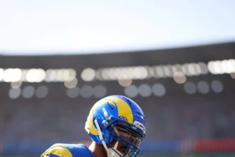 Myles Garrett - Ein Footballspieler in blau-gelbem Trikot und Helm steht während eines Spiels auf dem Spielfeld; im Hintergrund sind das Stadion und die Zuschauer zu sehen. Bericht Garrett wird am Knie behandelt, während er sich auf das nächste Spiel vorbereitet. Alt-Text wurde KI-generiert.