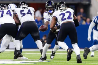 Lamar Jackson - Ein Quarterback im American Football übergibt den Ball während eines Spielzugs an einen Runningback, während im Hintergrund auf dem Spielfeld die Offensive Linemen die Verteidiger blocken – ein Bild, das die Intensität widerspiegelt, die man oft bei den Sonntagsspielen der ersten Woche der NFL sieht, und das Fans und Trainern gleichermaßen erste Erkenntnisse liefert. Alt-Text wurde KI-generiert.