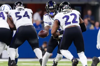NFL Woche 3 - Lamar Jackson - Ein Quarterback im American Football übergibt den Ball während eines Spielzugs an einen Runningback, während im Hintergrund auf dem Spielfeld die Offensive Linemen die Verteidiger blocken – ein Bild, das die Intensität widerspiegelt, die man oft bei den Sonntagsspielen der ersten Woche der NFL sieht, und das Fans und Trainern gleichermaßen erste Erkenntnisse liefert. Alt-Text wurde KI-generiert.