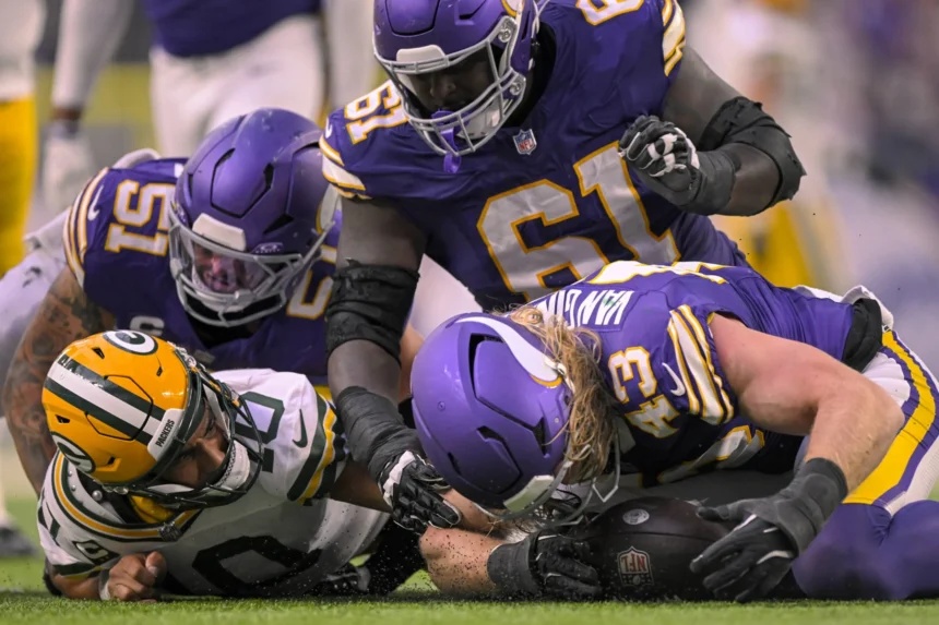 Offensive Line - Vier Footballspieler kämpfen während eines Spiels zwischen den Minnesota Vikings und den Green Bay Packers auf dem Spielfeld um einen freien Ball, während die Packers in diesem intensiven Duell der Rivalen nach Antworten suchen. Alt-Text wurde KI-generiert.