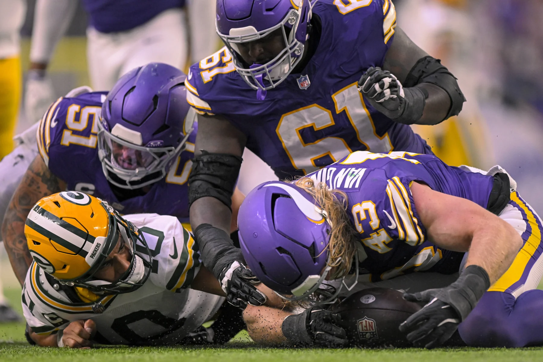 Offensive Line - Vier Footballspieler kämpfen während eines Spiels zwischen den Minnesota Vikings und den Green Bay Packers auf dem Spielfeld um einen freien Ball, während die Packers in diesem intensiven Duell der Rivalen nach Antworten suchen. Alt-Text wurde KI-generiert.