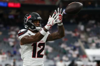 Nico Collins - Ein Footballspieler in einem weißen Trikot der Houston Texans mit der Nummer 12 fängt während eines Spiels einen Football, im Hintergrund sind verschwommene Stadionplätze zu sehen – dies unterstreicht den Moment, in dem Collins von den Texans gegen die Bengals ausfällt. Alt-Text wurde KI-generiert.