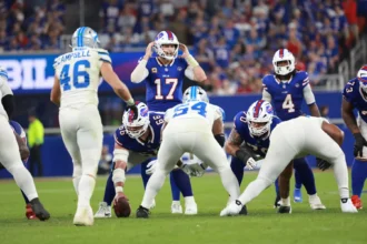 Josh Allen, der Quarterback der Buffalo Bills, erzielt 5 Touchdowns, während er sich darauf vorbereitet, den Snap zu empfangen, und dabei den Verteidigern der Carolina Panthers gegenübersteht. Alt-Text wurde KI-generiert.