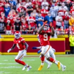 Kenneth Walker - Ein Footballspieler in roter Spielkleidung macht sich während eines Spiels bereit, einen Pass zu fangen, was an die spannenden Momente erinnert, in denen Mahomes und die Chiefs ihre größten Herausforderungen meistern – mit Teamkollegen, Gegnern und dem Publikum im Hintergrund. Alt-Text wurde KI-generiert.