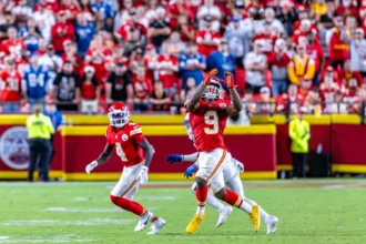 Kenneth Walker - Ein Footballspieler in roter Spielkleidung macht sich während eines Spiels bereit, einen Pass zu fangen, was an die spannenden Momente erinnert, in denen Mahomes und die Chiefs ihre größten Herausforderungen meistern – mit Teamkollegen, Gegnern und dem Publikum im Hintergrund. Alt-Text wurde KI-generiert.