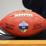 Rio de Janeiro - Ein Wilson-NFL-Football mit der Aufschrift „The Duke“ und einem „RIO GAME“-Aufkleber liegt auf einem Tisch; auf dem Ball sind Unterschriften und Logos zu sehen – Kein Grund zur Sorge, dieses wertvolle Sammlerstück ist gut geschützt und bereit für die Ausstellung. Alt-Text wurde KI-generiert.