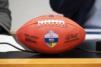 Rio de Janeiro - Ein Wilson-NFL-Football mit der Aufschrift „The Duke“ und einem „RIO GAME“-Aufkleber liegt auf einem Tisch; auf dem Ball sind Unterschriften und Logos zu sehen – Kein Grund zur Sorge, dieses wertvolle Sammlerstück ist gut geschützt und bereit für die Ausstellung. Alt-Text wurde KI-generiert.