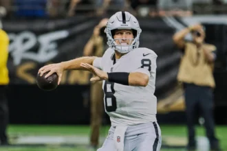 NFL Week 3 - Kirk Cousins - Ein Footballspieler im weißen Trikot der Las Vegas Raiders bereitet sich während eines Spiels der dritten NFL-Runde auf einen Pass vor, im Hintergrund sind Fotografen und Fans zu sehen – sie halten einige der wichtigsten Erkenntnisse dieses Sonntagsspiels fest. Alt-Text wurde KI-generiert.