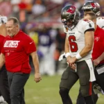 Baker Mayfield - Ein Footballspieler im Trikot der Buccaneers verlässt während eines Spiels zusammen mit Trainern und Betreuern das Spielfeld, hält sich den Arm und scheint verletzt zu sein – Mayfield fällt wegen einer Daumenverletzung mindestens für den Rest des Spiels aus. Alt-Text wurde KI-generiert.
