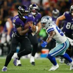 Rio de Janeiro - Ein Spieler der Ravens in lila rennt mit dem Football davon, während er von einem Verteidiger der Dallas Cowboys in weiß und blau verfolgt wird; im Hintergrund sind weitere Spieler der Ravens und der Cowboys zu sehen. Alt-Text wurde KI-generiert.