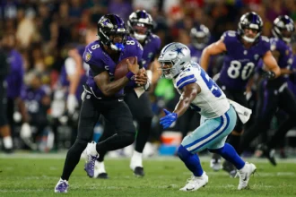 Rio de Janeiro - Ein Spieler der Ravens in lila rennt mit dem Football davon, während er von einem Verteidiger der Dallas Cowboys in weiß und blau verfolgt wird; im Hintergrund sind weitere Spieler der Ravens und der Cowboys zu sehen. Alt-Text wurde KI-generiert.