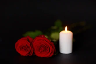 Zwei rote Southern-Nazarene-Rosen und eine brennende weiße Kerze auf dunklem Hintergrund.