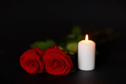 Zwei rote Southern-Nazarene-Rosen und eine brennende weiße Kerze auf dunklem Hintergrund.