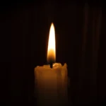 Eine brennende Kerze mit einer leuchtenden Flamme vor einem dunklen Hintergrund.