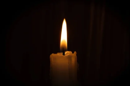 Eine brennende Kerze mit einer leuchtenden Flamme vor einem dunklen Hintergrund.