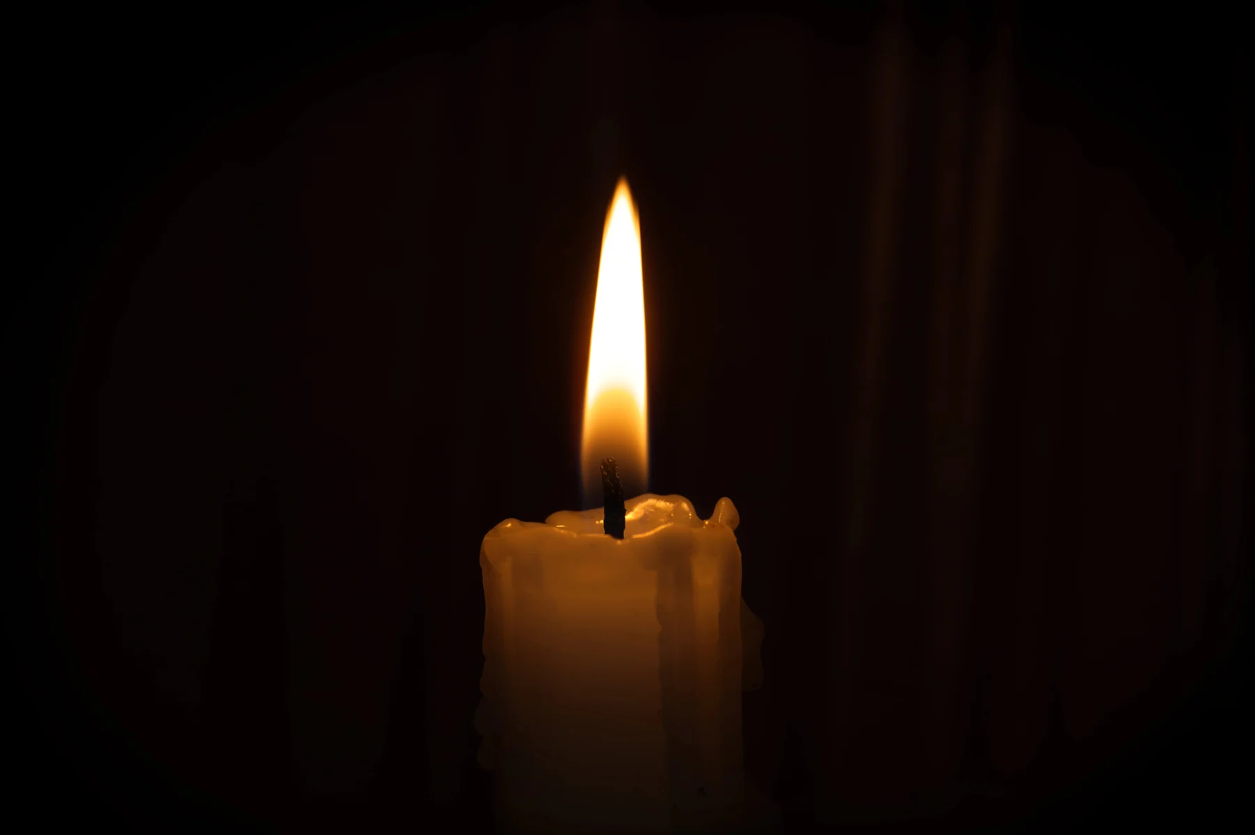 Eine brennende Kerze mit einer leuchtenden Flamme vor einem dunklen Hintergrund.