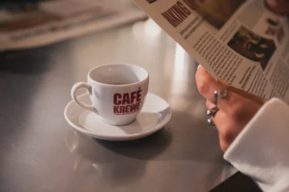 Eine Tasse Café Krewe-Kaffee steht auf einer Untertasse neben einer Person, die im „Buccaneers Café“ eine Zeitung liest.