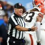 Ein NFL Schiedsrichter, einer von zwei kürzlich suspendierten Offiziellen, gestikuliert, während er auf dem Spielfeld mit einem Spieler der Cleveland Browns spricht. Alt-Text wurde KI-generiert.