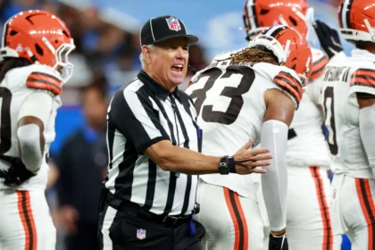 Ein NFL Schiedsrichter, einer von zwei kürzlich suspendierten Offiziellen, gestikuliert, während er auf dem Spielfeld mit einem Spieler der Cleveland Browns spricht. Alt-Text wurde KI-generiert.