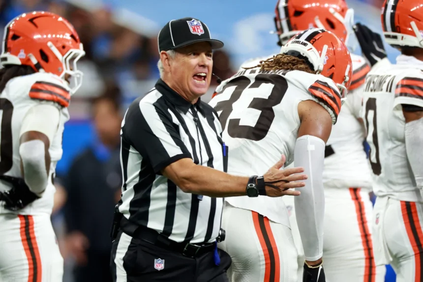 Ein NFL Schiedsrichter, einer von zwei kürzlich suspendierten Offiziellen, gestikuliert, während er auf dem Spielfeld mit einem Spieler der Cleveland Browns spricht. Alt-Text wurde KI-generiert.
