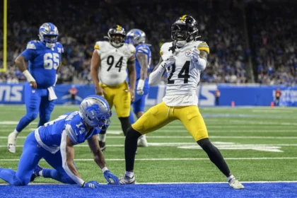 Joey Porter Jr. feiert in der Endzone, während ein Verteidiger der Detroit Lions während eines Footballspiels auf dem Rasen kniet. Alt-Text wurde KI-generiert.