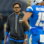 Mike McDaniel - Ein Trainer in einem dunkelgrauen Hoodie der Los Angeles Chargers steht auf dem Spielfeld neben seinen Chargers-Spielern.