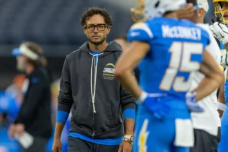 Mike McDaniel - Ein Trainer in einem dunkelgrauen Hoodie der Los Angeles Chargers steht auf dem Spielfeld neben seinen Chargers-Spielern.