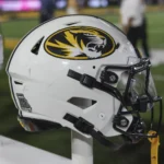 Johnnie DJ Jones Weißer Football-Helm der Missouri Tigers für den Studienanfänger Johnnie, mit einem Tiger-Logo und einem Aufkleber mit den Umrissen des Bundesstaates auf einem Ständer. Alt-Text wurde KI-generiert.