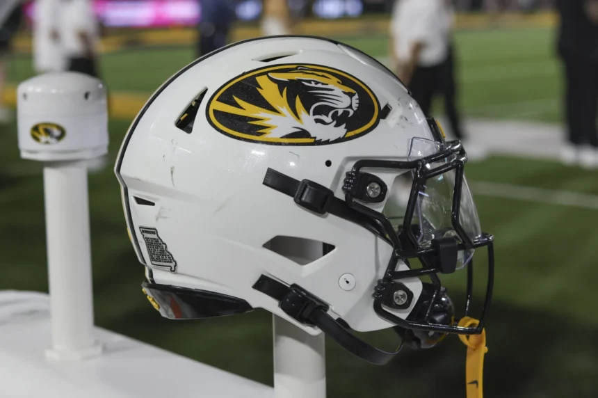 Johnnie DJ Jones Weißer Football-Helm der Missouri Tigers für den Studienanfänger Johnnie, mit einem Tiger-Logo und einem Aufkleber mit den Umrissen des Bundesstaates auf einem Ständer. Alt-Text wurde KI-generiert.