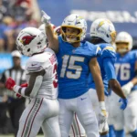 Ladd McConkey - Ein Footballspieler in einem blauen Chargers-Trikot zeigt nach oben, während er während eines Spiels neben McConkey in einem weißen Trikot steht. Alt-Text wurde KI-generiert.