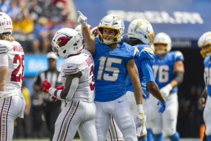 Ladd McConkey - Ein Footballspieler in einem blauen Chargers-Trikot zeigt nach oben, während er während eines Spiels neben McConkey in einem weißen Trikot steht. Alt-Text wurde KI-generiert.
