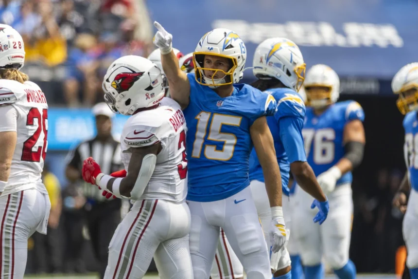 Ladd McConkey - Ein Footballspieler in einem blauen Chargers-Trikot zeigt nach oben, während er während eines Spiels neben McConkey in einem weißen Trikot steht. Alt-Text wurde KI-generiert.