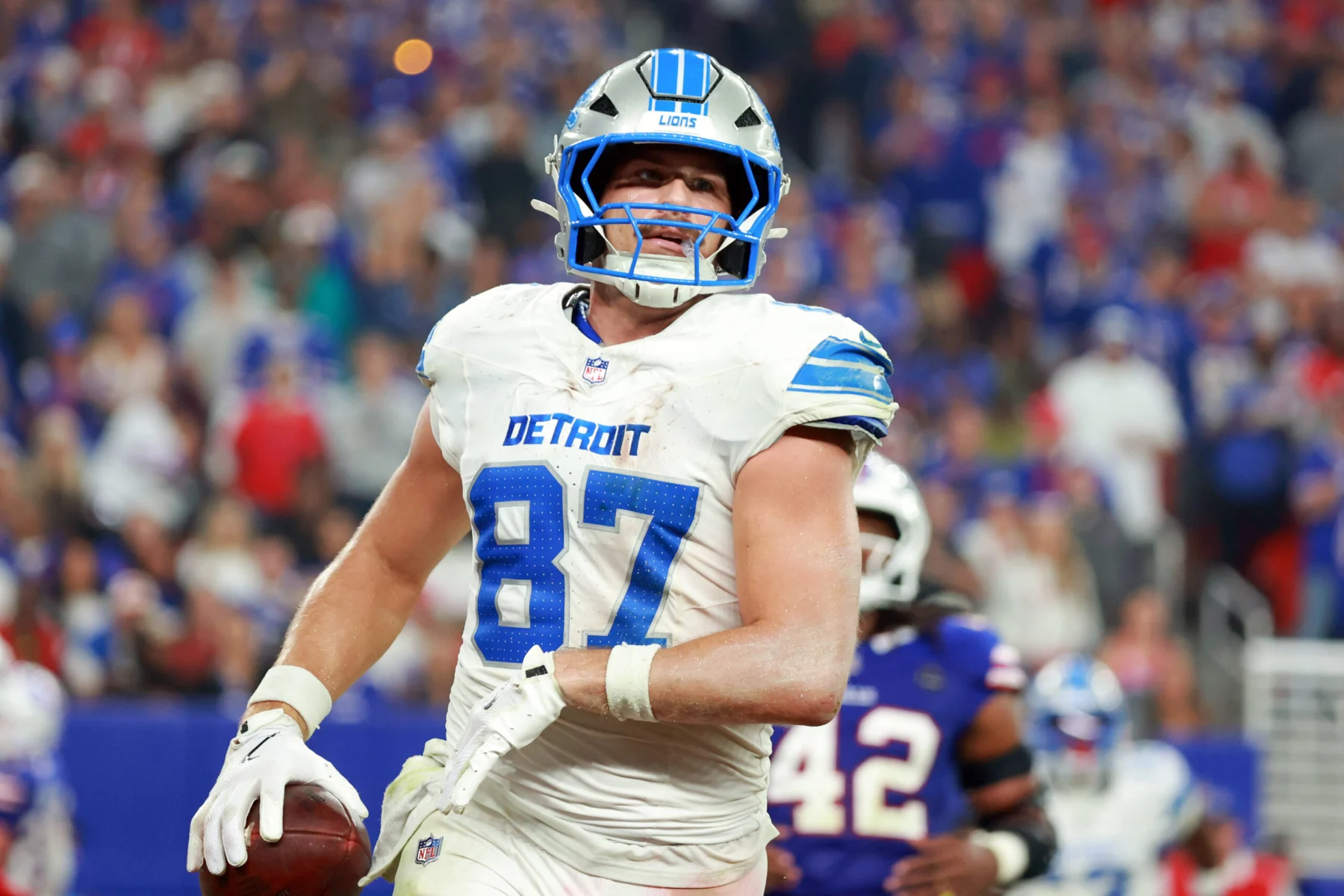 Detroit Lions player Sam LaPorta holds a football during a game while wearing his white jersey.