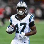 Xavier Legette - Ein Footballspieler in einem weißen Trikot der Carolina Panthers hält einen Football in der Hand, während er über das Spielfeld läuft, nachdem die Panthers Legette im Rahmen einer neuen Strategie eingesetzt haben. Alt-Text wurde KI-generiert.