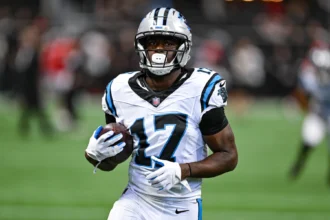 Xavier Legette - Ein Footballspieler in einem weißen Trikot der Carolina Panthers hält einen Football in der Hand, während er über das Spielfeld läuft, nachdem die Panthers Legette im Rahmen einer neuen Strategie eingesetzt haben. Alt-Text wurde KI-generiert.