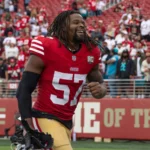 Dre Greenlaw, Spieler der San Francisco 49ers, lächelt und rennt vor seiner Ein-Spiele-Sperre über das Spielfeld. Alt-Text wurde KI-generiert.
