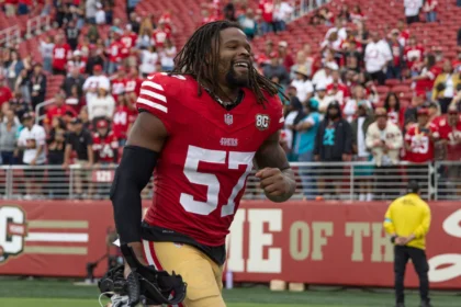 Dre Greenlaw, Spieler der San Francisco 49ers, lächelt und rennt vor seiner Ein-Spiele-Sperre über das Spielfeld. Alt-Text wurde KI-generiert.