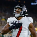 Bijan Robinson - Ein Spieler der Atlanta Falcons im Trikot mit der Nummer 7, der während des „Monday Night Football“ die Hand auf das Herz legt. Alt-Text wurde KI-generiert.