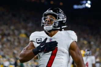 Bijan Robinson - Ein Spieler der Atlanta Falcons im Trikot mit der Nummer 7, der während des „Monday Night Football“ die Hand auf das Herz legt. Alt-Text wurde KI-generiert.