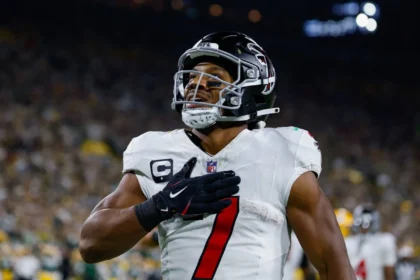 Bijan Robinson - Ein Spieler der Atlanta Falcons im Trikot mit der Nummer 7, der während des „Monday Night Football“ die Hand auf das Herz legt. Alt-Text wurde KI-generiert.