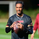 Commanders-Quarterback Jayden Daniels hält einen Football in der Hand und trägt dabei eine schwarze Armbandage. Alt-Text wurde KI-generiert.
