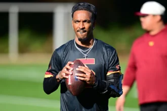 Commanders-Quarterback Jayden Daniels hält einen Football in der Hand und trägt dabei eine schwarze Armbandage. Alt-Text wurde KI-generiert.