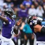 Lamar Jackson, Quarterback der Baltimore Ravens, bereitet sich während des „Sunday Night Football“-Spiels auf einen Pass vor, während ein Teamkollege einen Spieler der Tennessee Titans blockt. Alt-Text wurde KI-generiert.