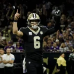 Tyler Shough, Quarterback der New Orleans Saints, steht mit erhobenen Armen neben Tyler Shough auf dem Spielfeld.